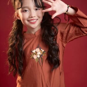 Smiling Vietnamese girl in traditional attire posing against a red background.
